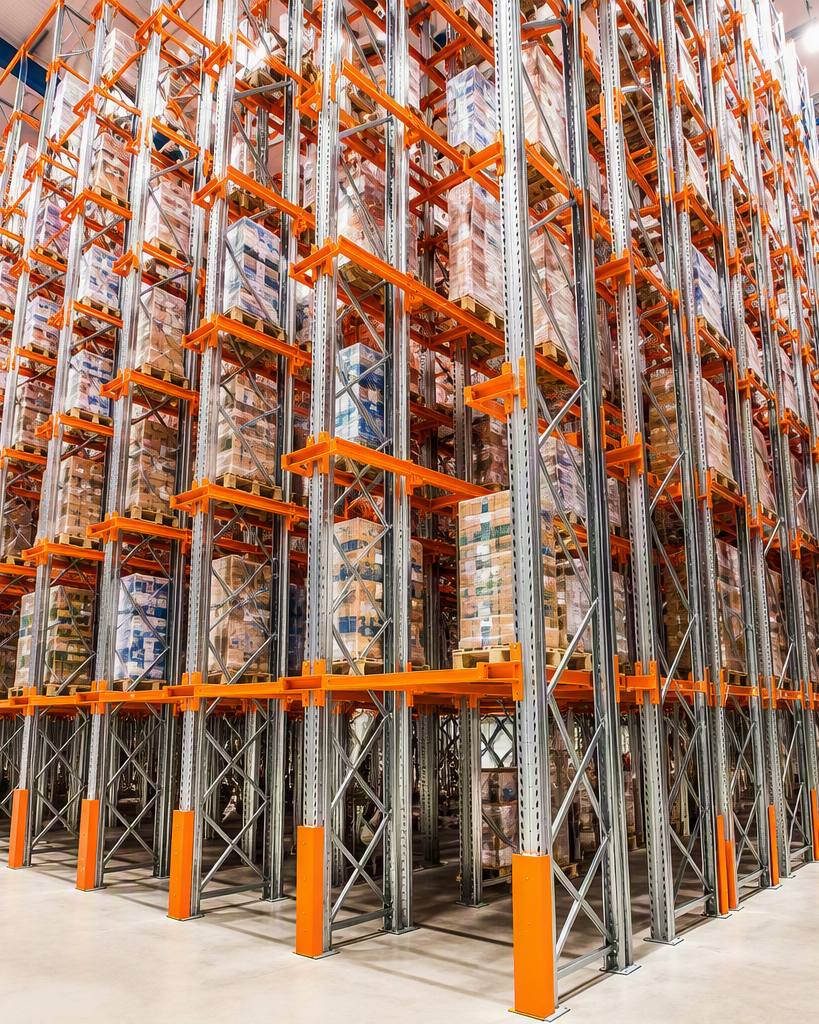 Tall pallet racking block holding stock several pallets deep with no aisles between the lanes