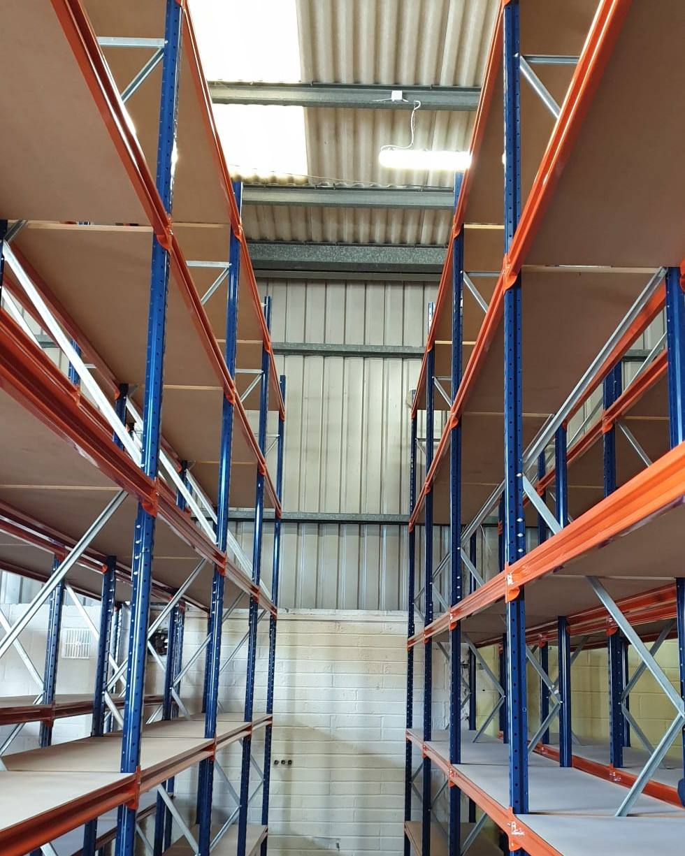 Aisle between two long span shelving runs with timber levels, seen from the end