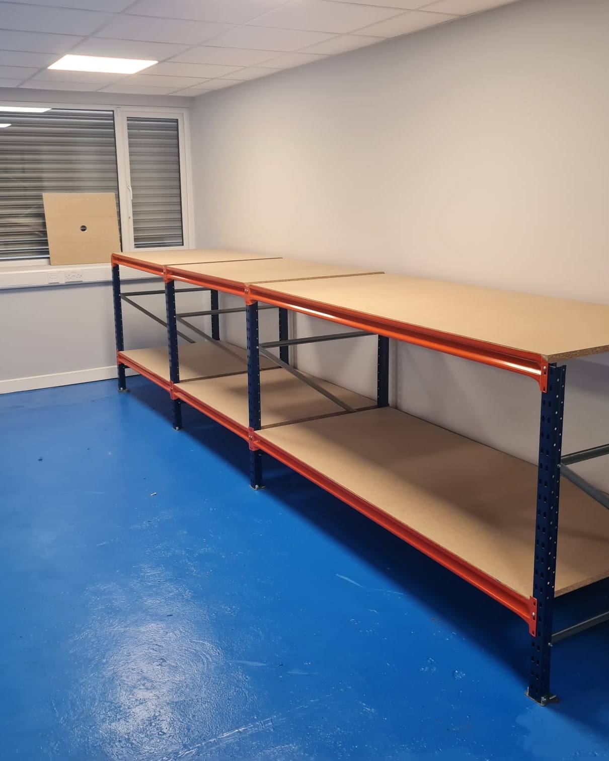 Long workbench with a timber top and a lower shelf, standing against the wall of a workshop